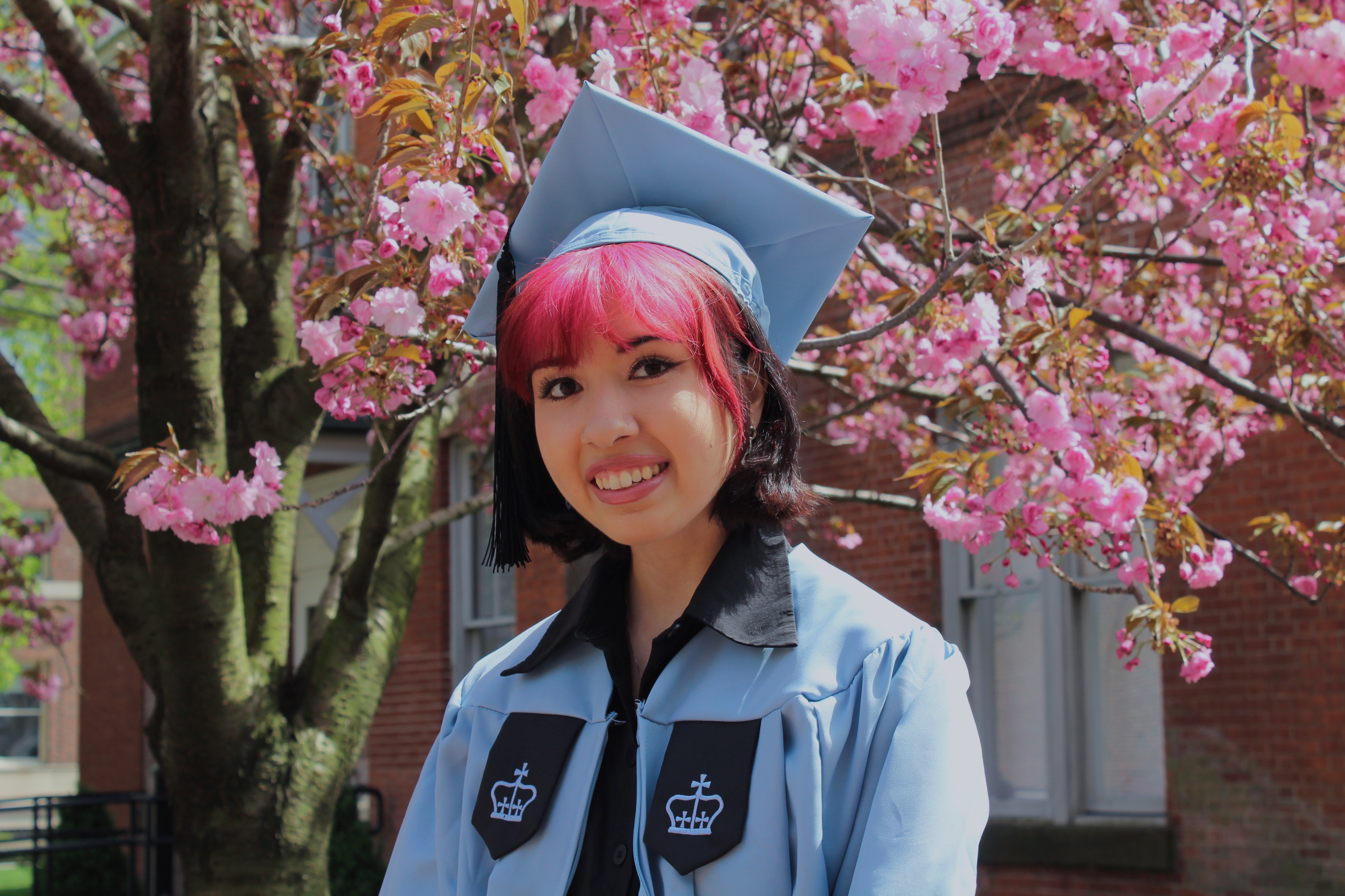 Barbara posing in front of a magnolia tree in her cap and gown