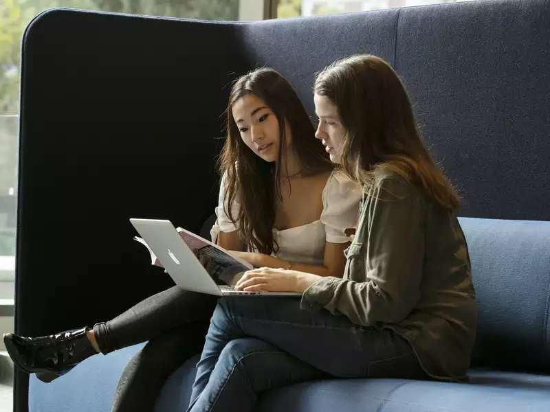 2 female students sit next to each other, using a laptop