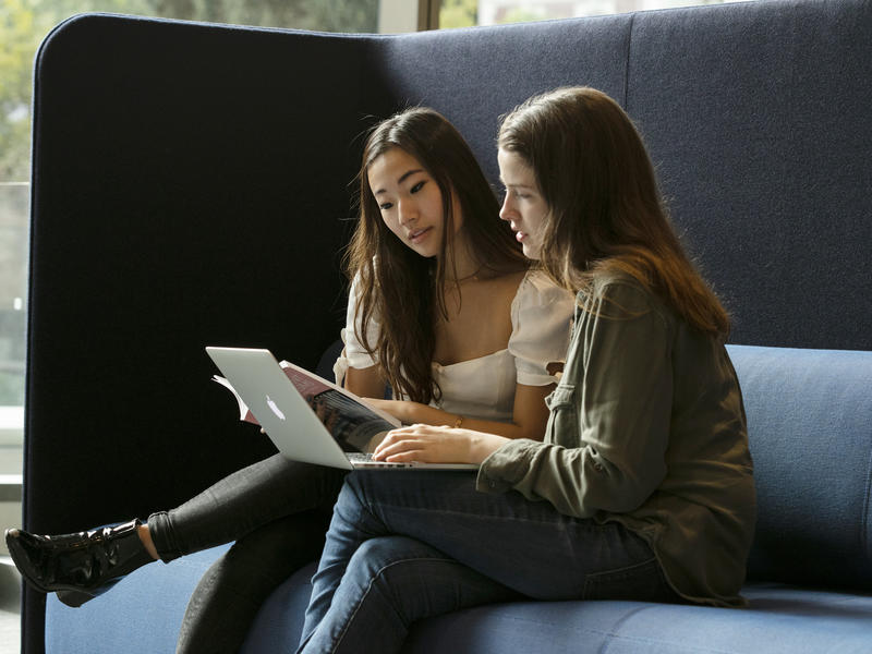 2 female students sit next to each other, using a laptop